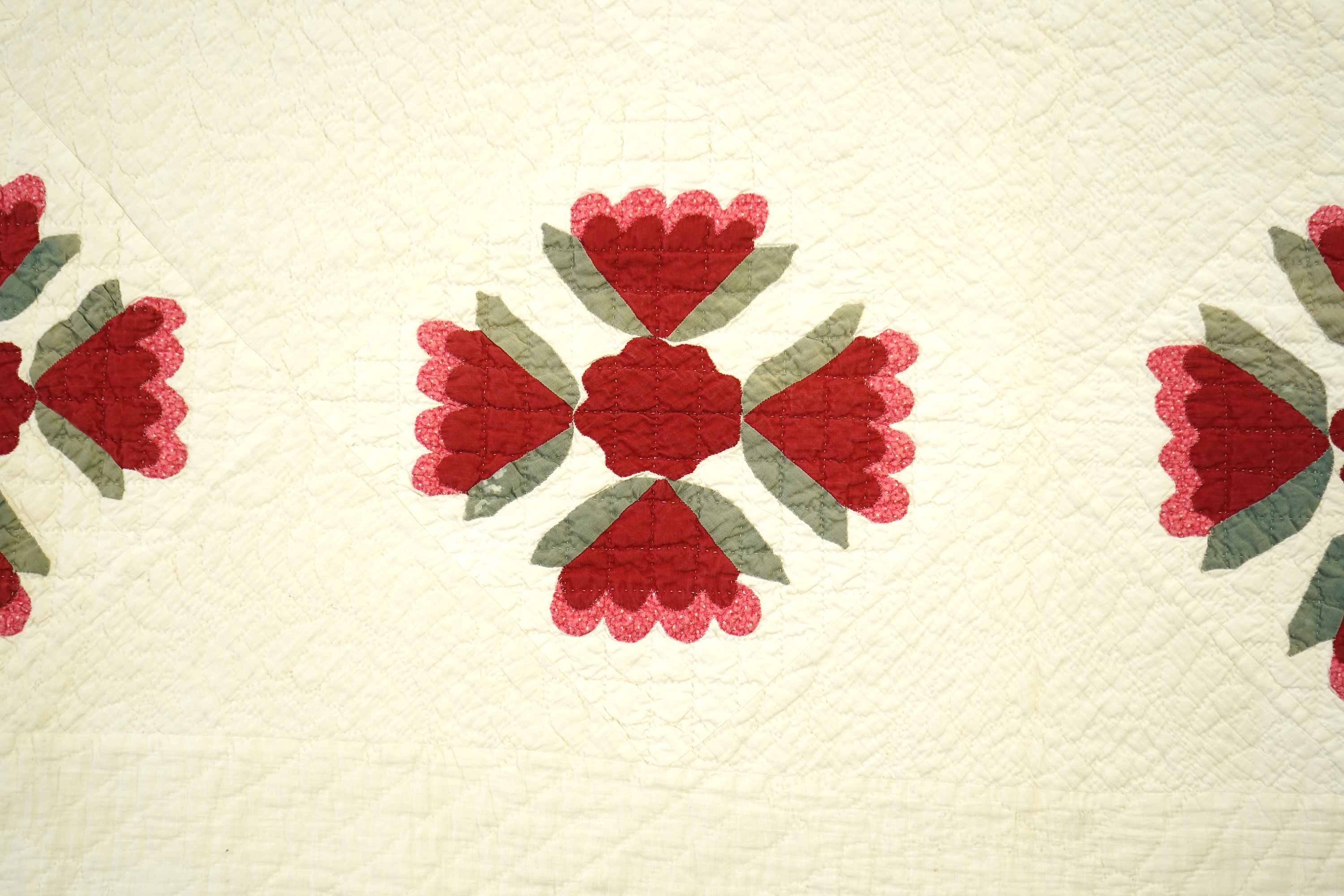 An American quilt from Kentucky, circa 1900. Intricately hand quilted on a white ground, appliquéd with stylistic repeating floral motifs in strong red and green cottons, all hand pieced. This quilt is a fine example of